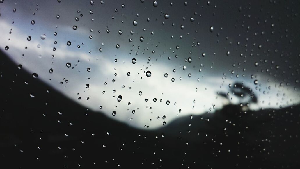 Close-up of waterdrops on glass against silhouette landscape