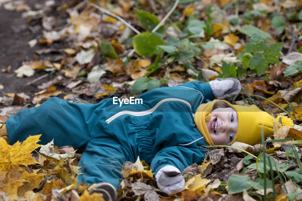 Little kid lying in autumn leaves having fun in forest