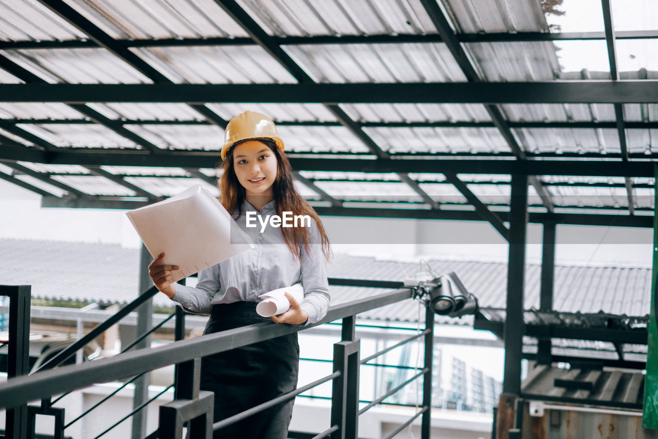 Portrait of young engineer holding blueprint while standing at site