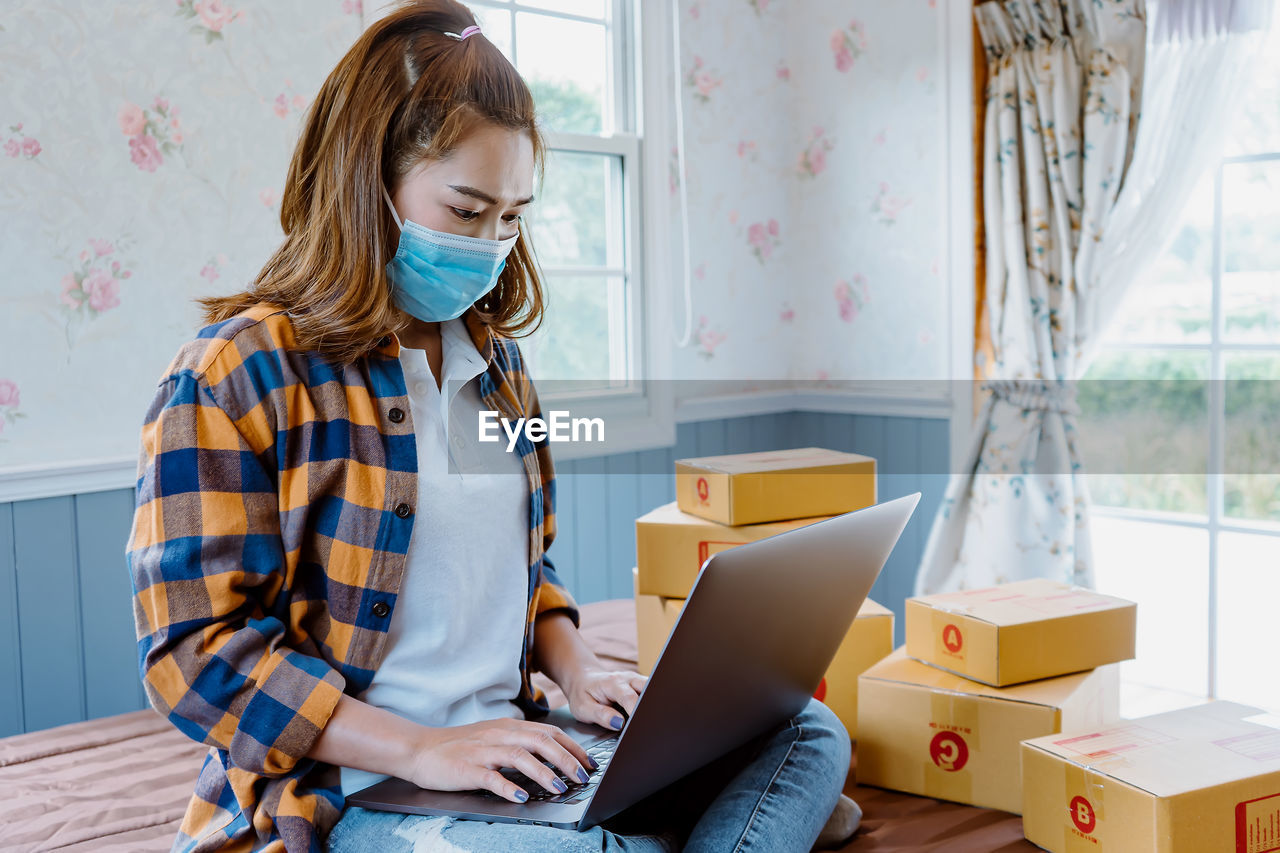 Asian woman at home using laptop to sell products online.