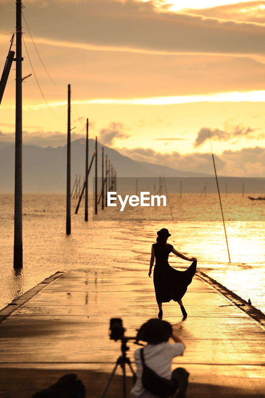 Rear view of people on wooden pier over sea against sky during sunset