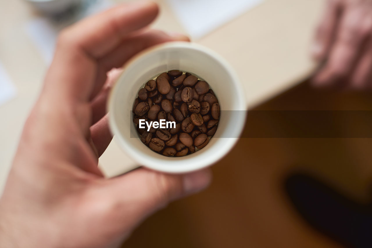 Close-up of hand holding cup of coffee beans