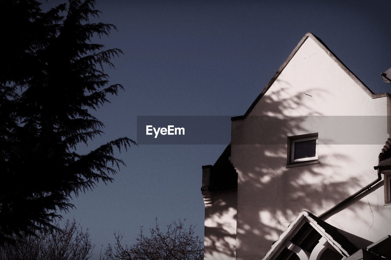 Low angle view of silhouette trees by house during sunny day