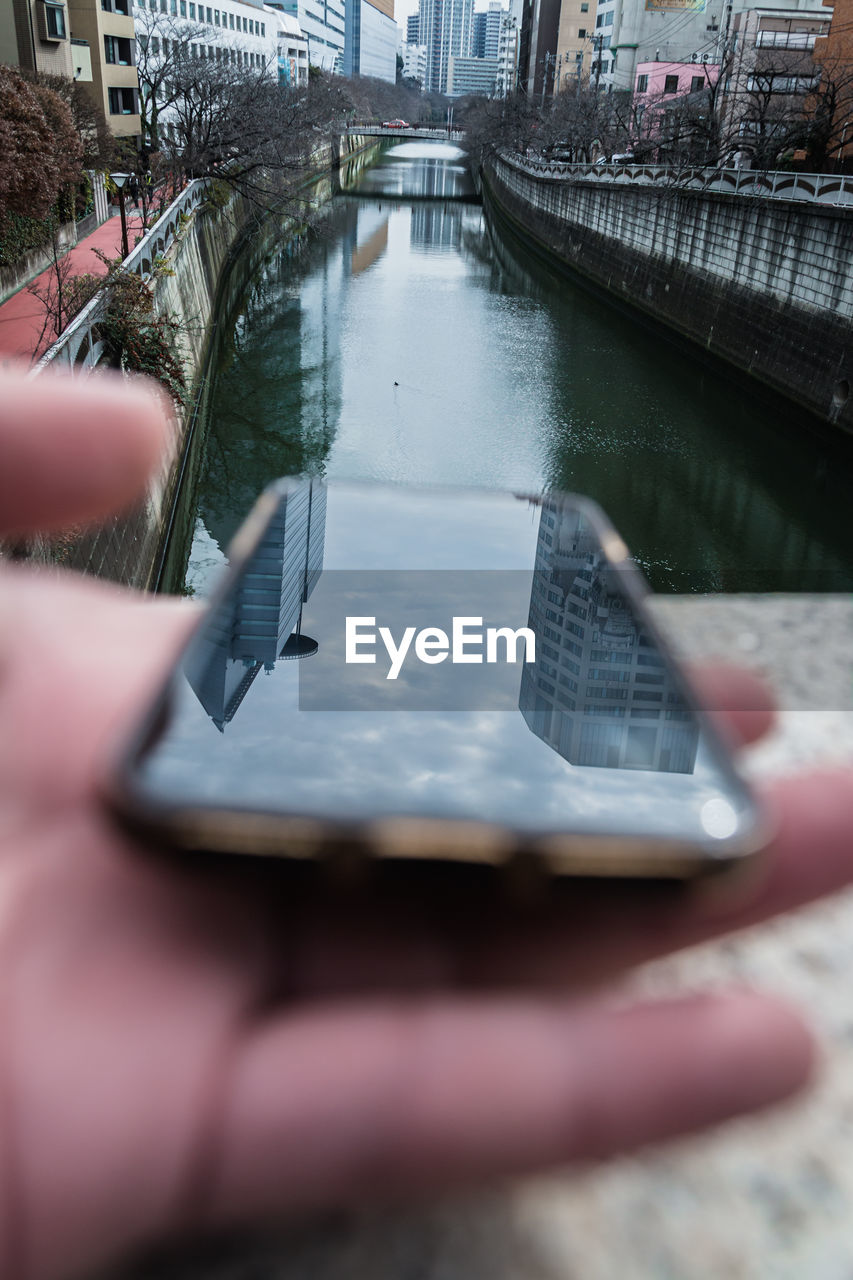 Smartphone screen reflects sky against river in city