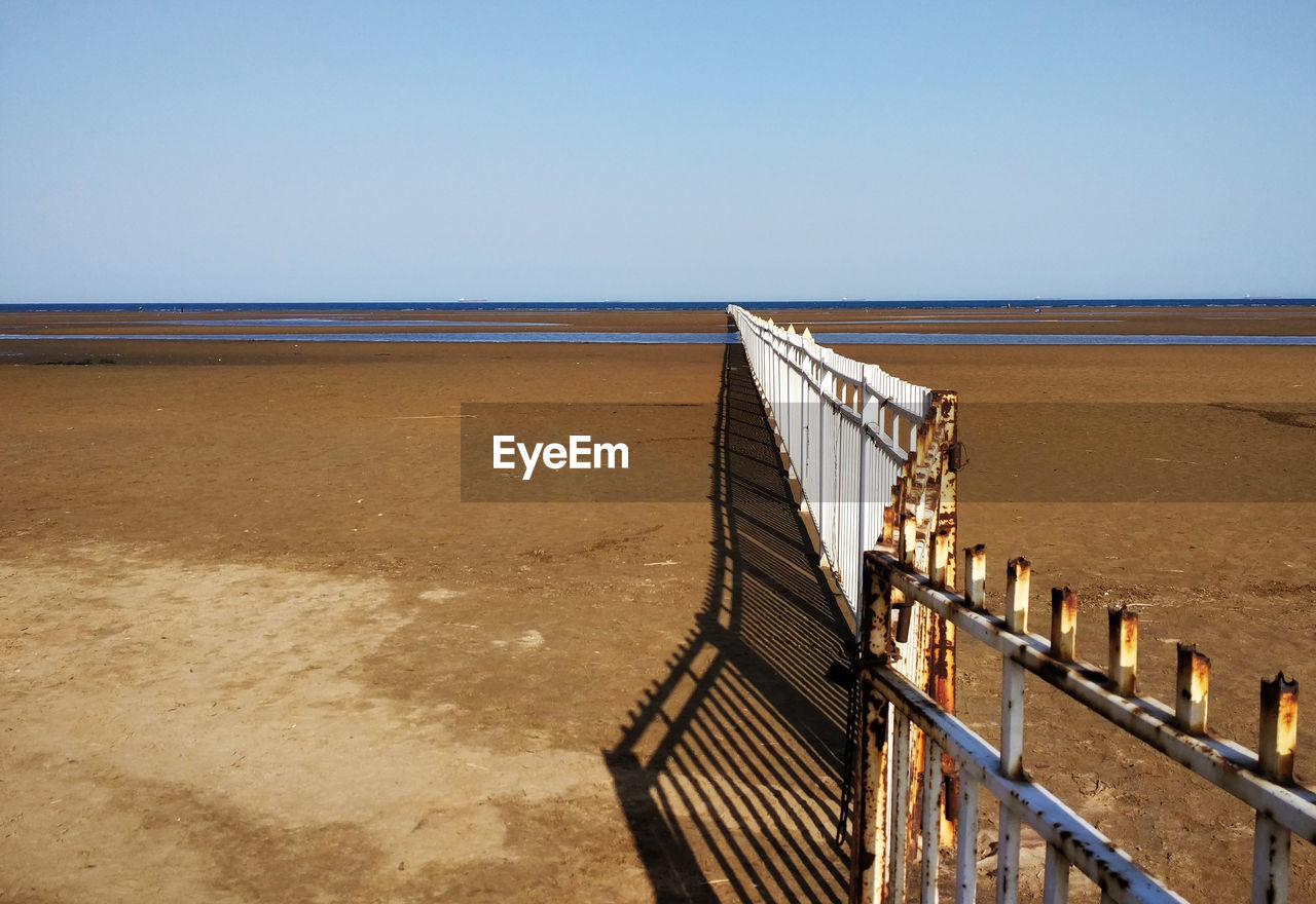 Wooden railing on beach against clear sky