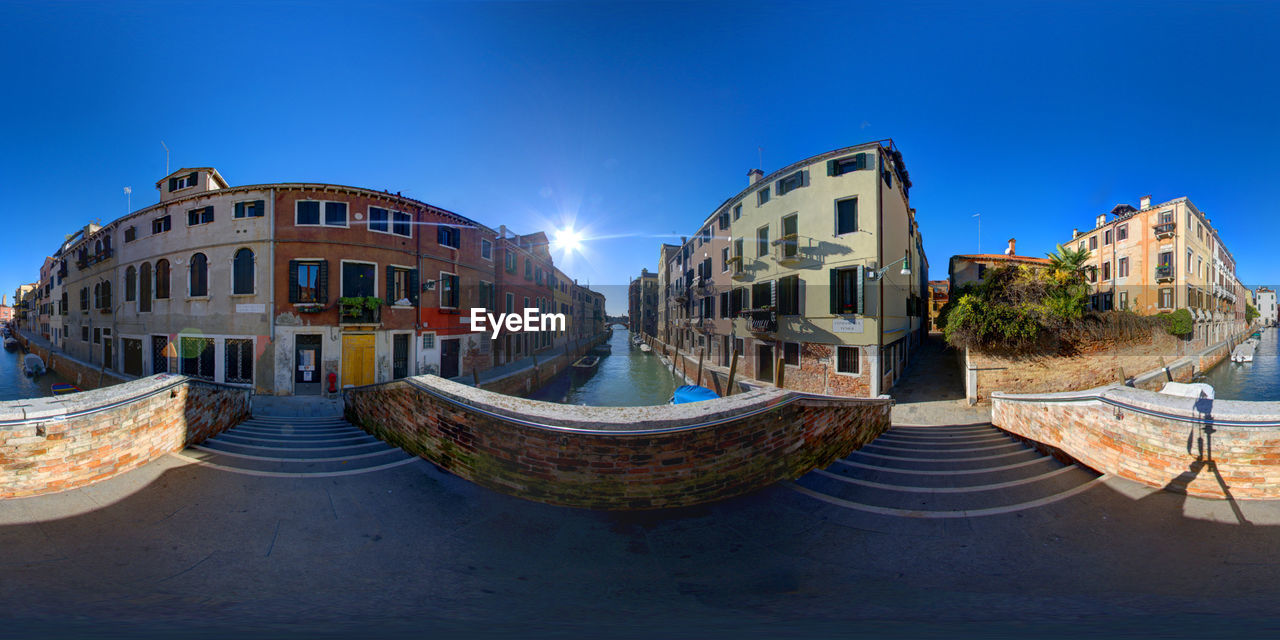 Fish-eye view of canal amidst buildings in city against clear sky