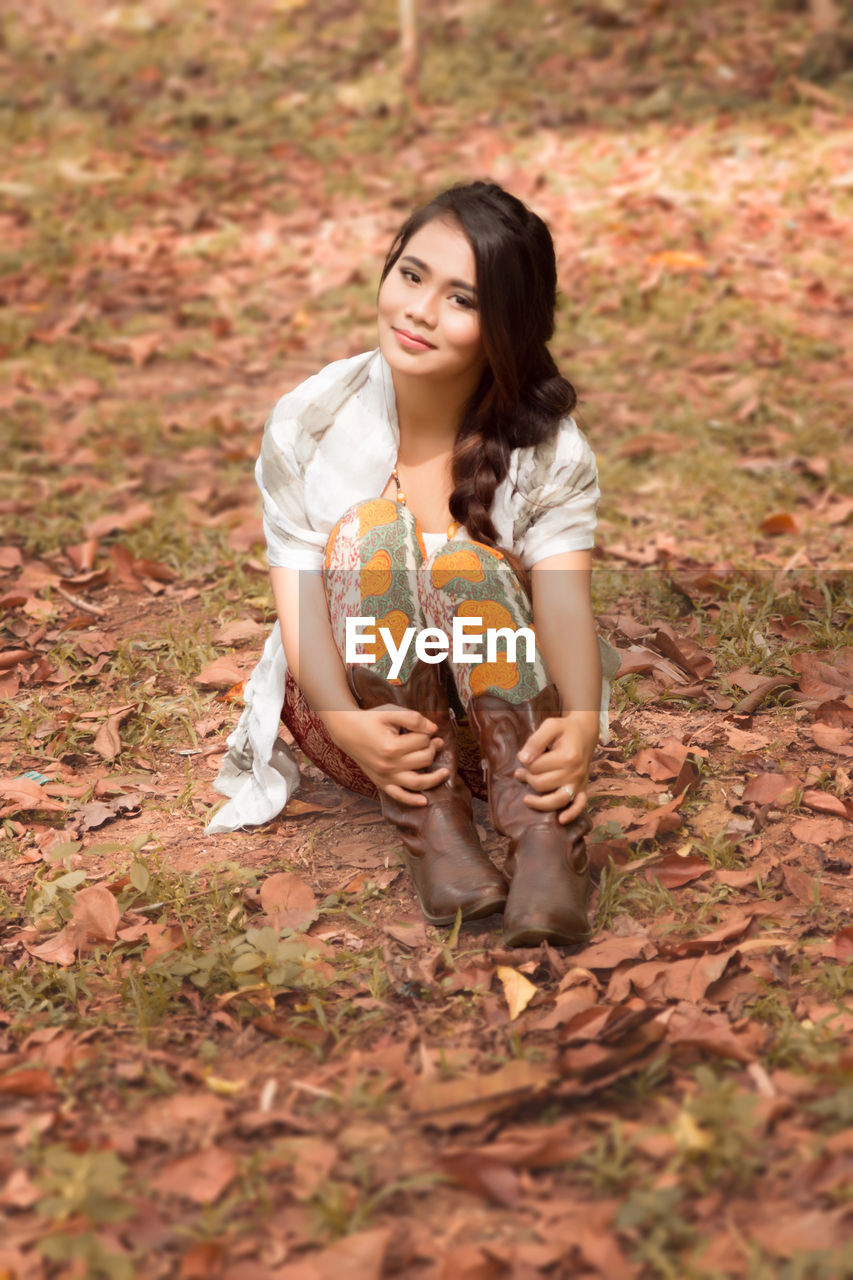 PORTRAIT OF YOUNG WOMAN SITTING ON AUTUMN