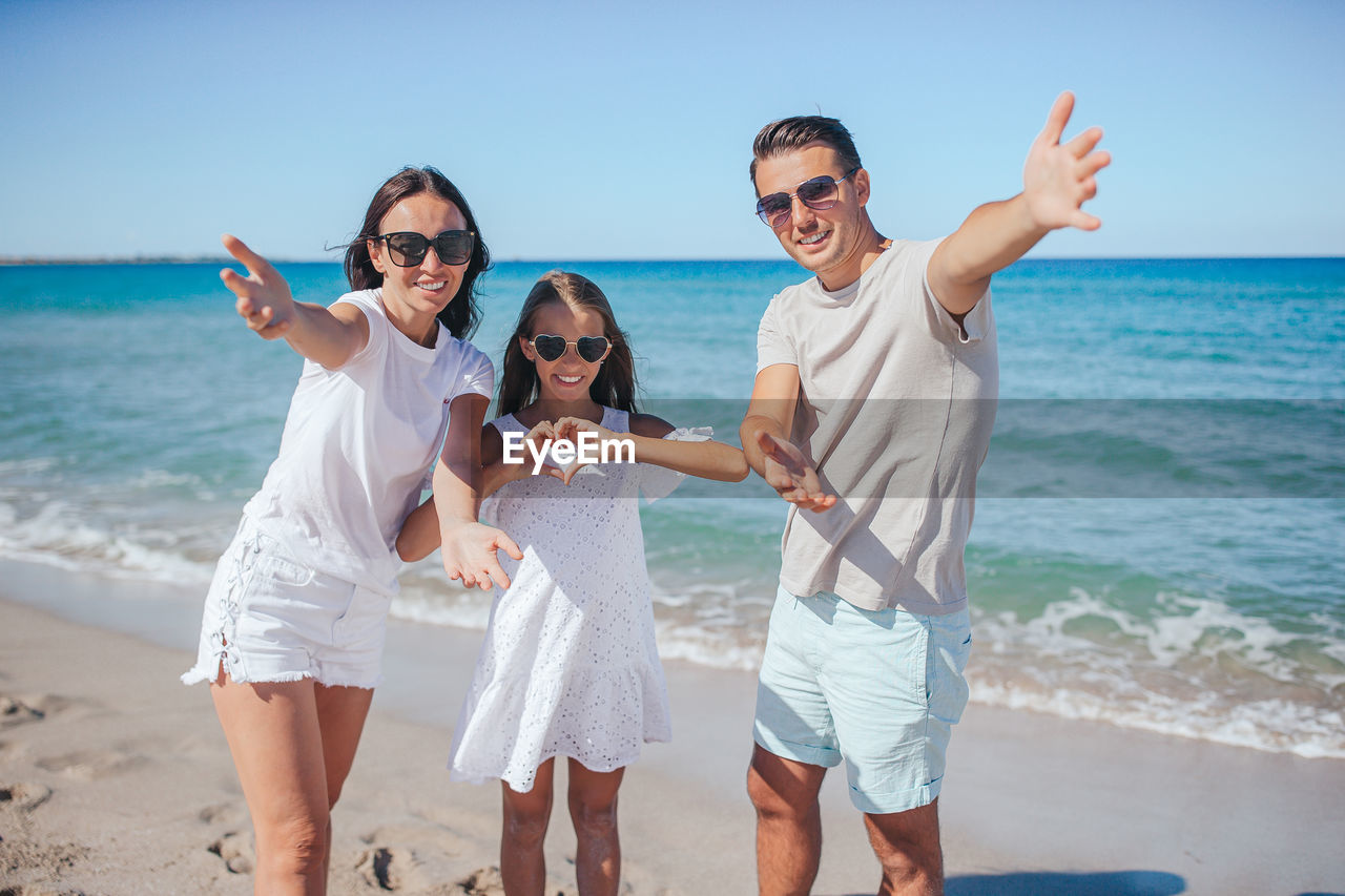 happy friends standing at beach against sky