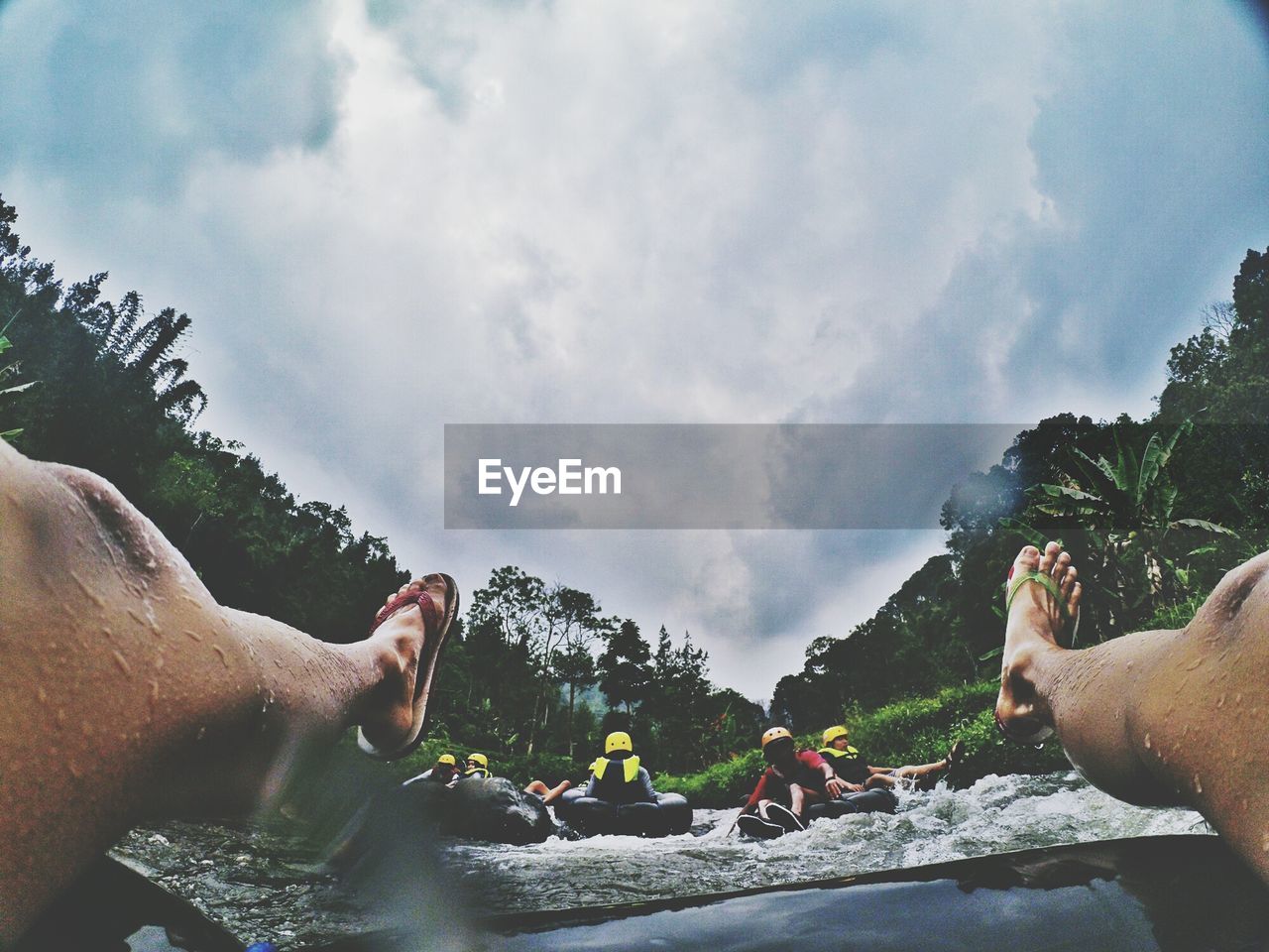 Low section of man river rafting on inflatable ring against cloudy sky