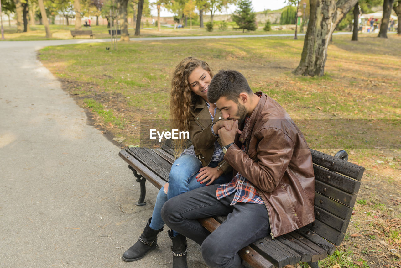 Boyfriend kissing girlfriend hand while sitting on park bench