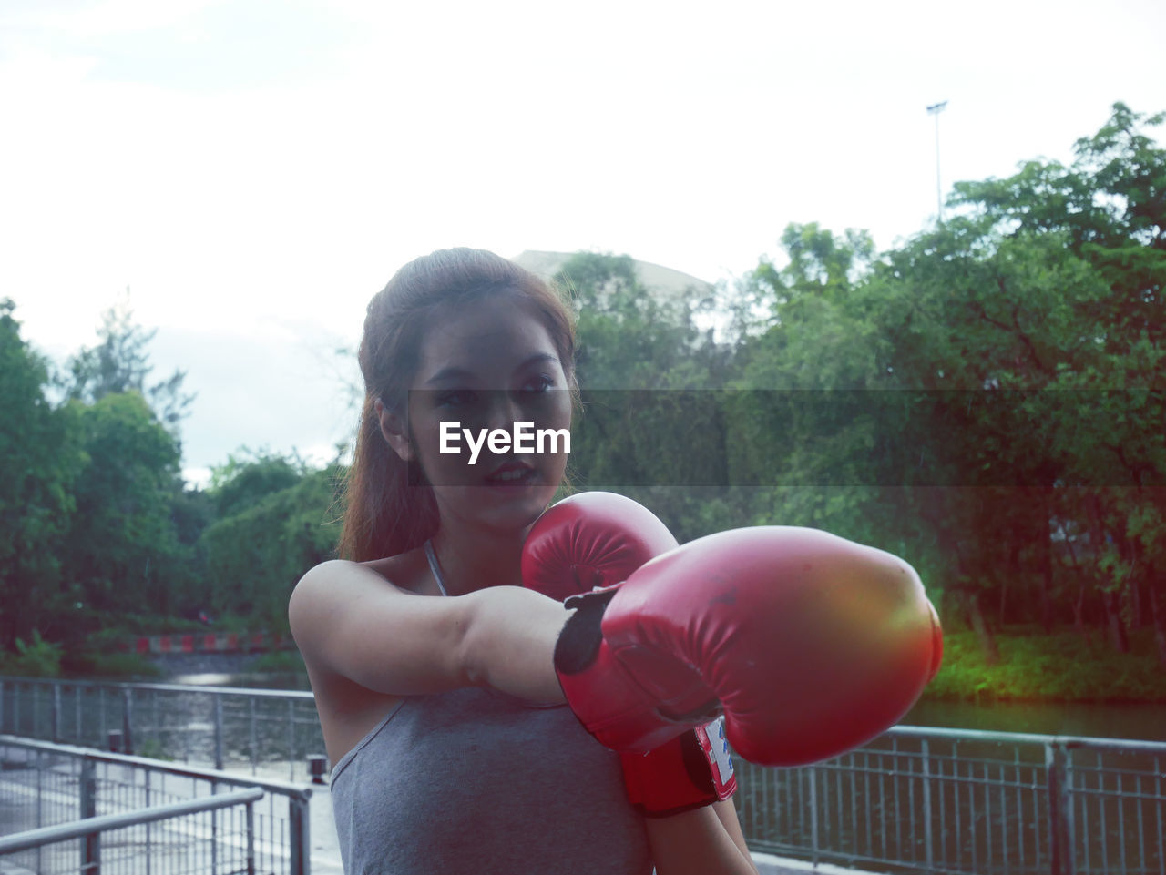 Young woman wearing boxing gloves while standing against trees