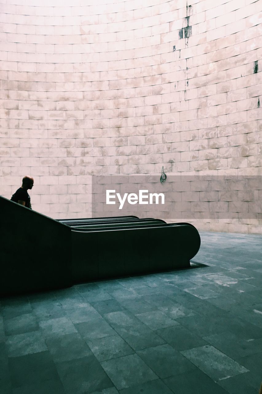 Man on escalator against stone wall