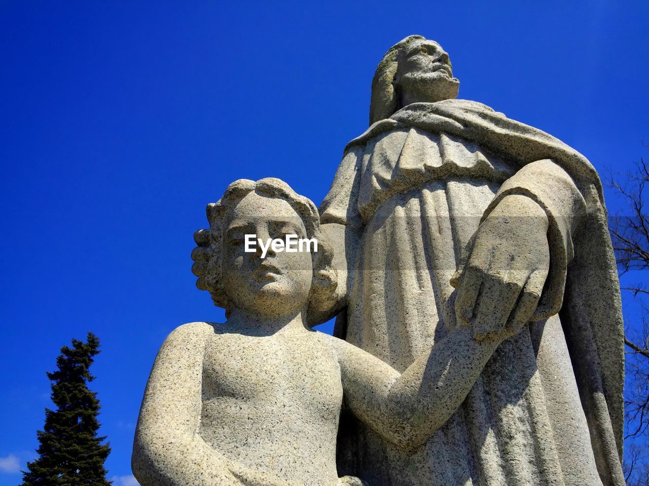 Low angle view of old statue of jesus and child against blue sky.