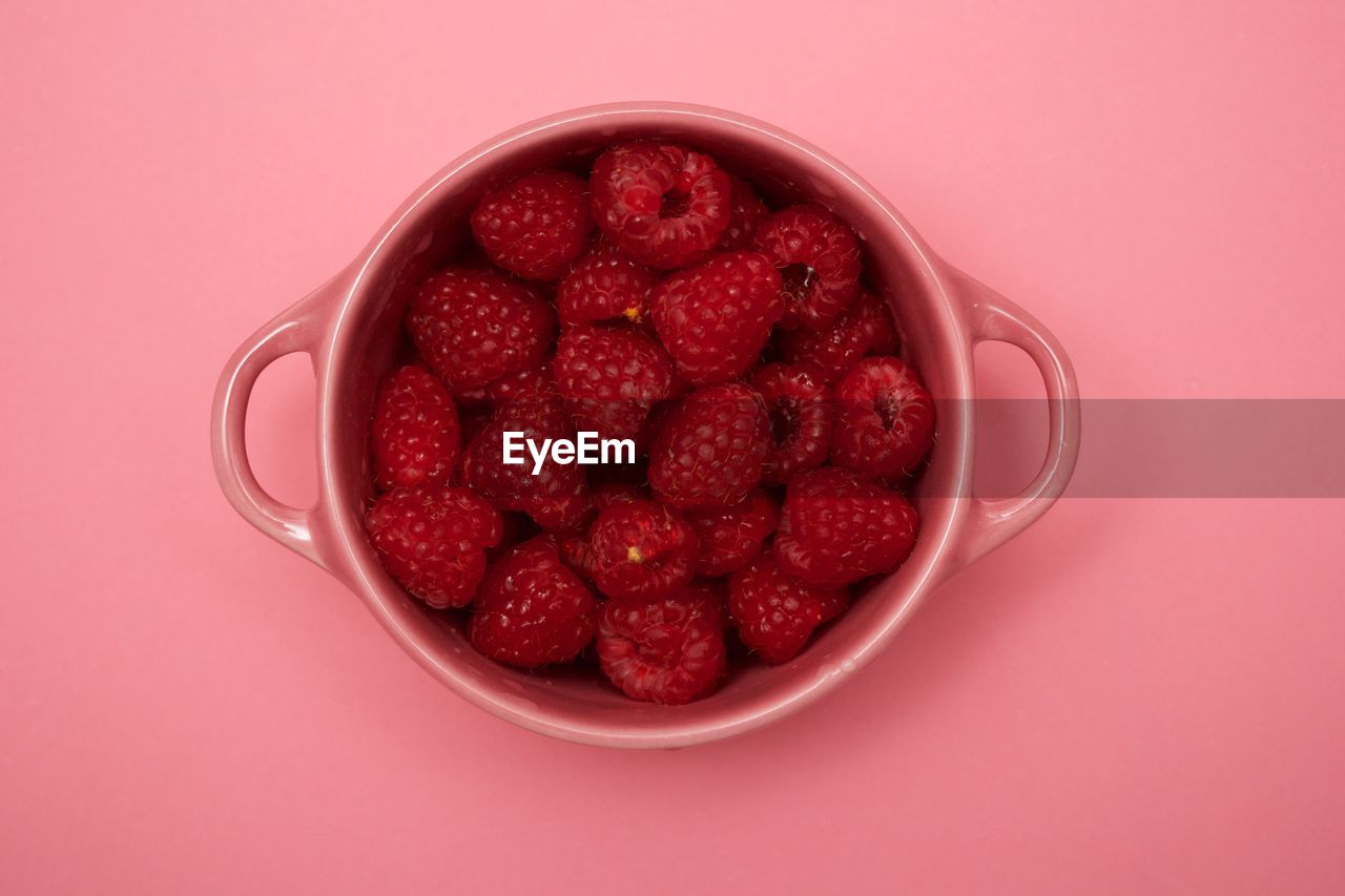 Directly above shot of raspberries in bowl over pink background