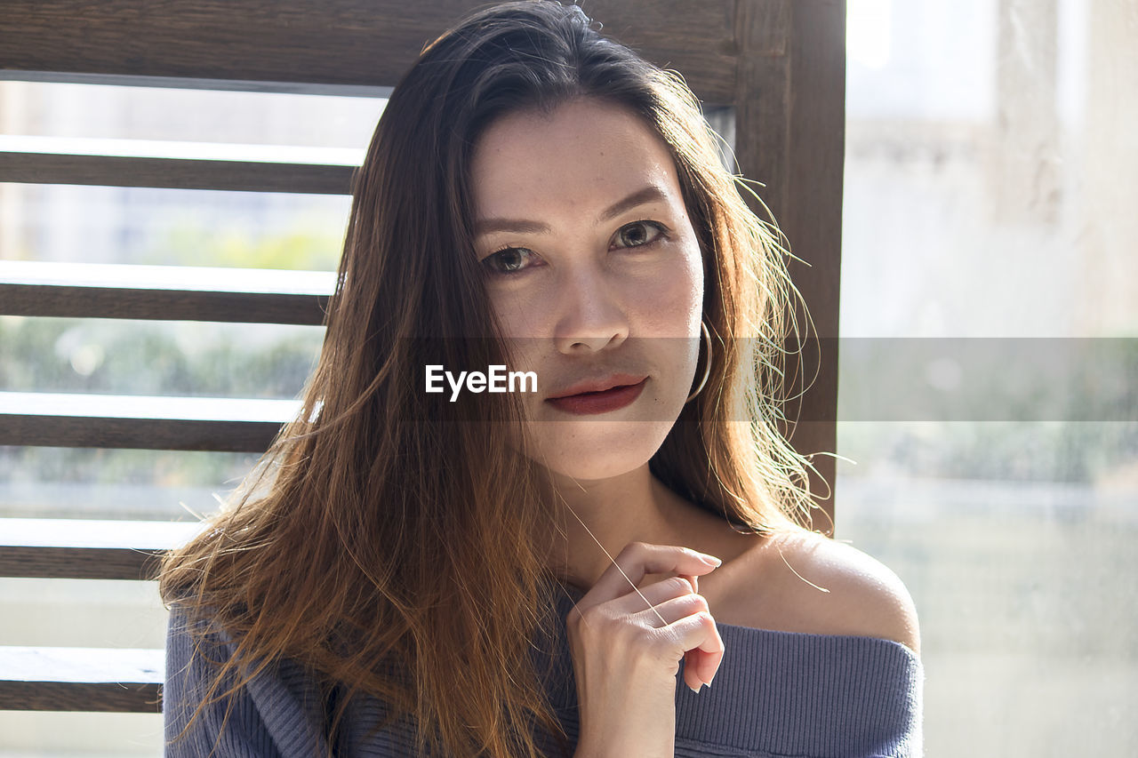 Close-up portrait of mid adult woman standing by window at home