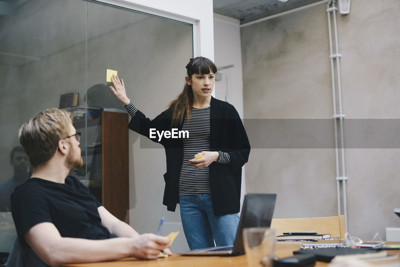 Female computer programmer showing adhesive note while giving presentation to colleague in office