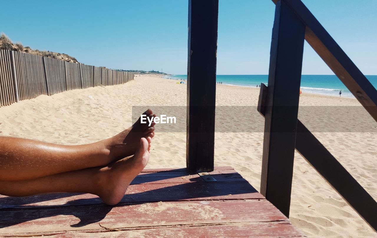 LOW SECTION OF PERSON RELAXING ON BEACH AGAINST SKY