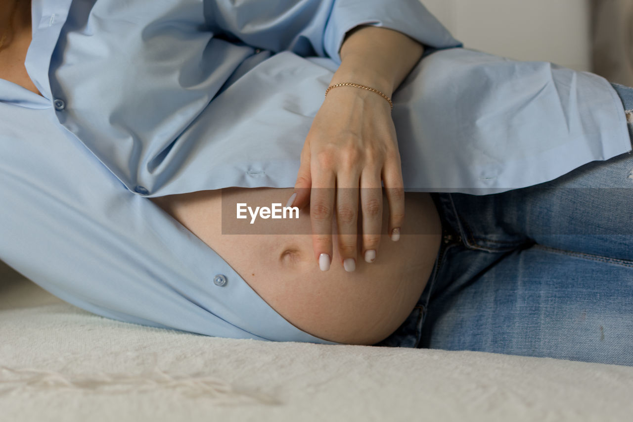 A pregnant woman is lying on her side on the sofa, her tummy is visible.