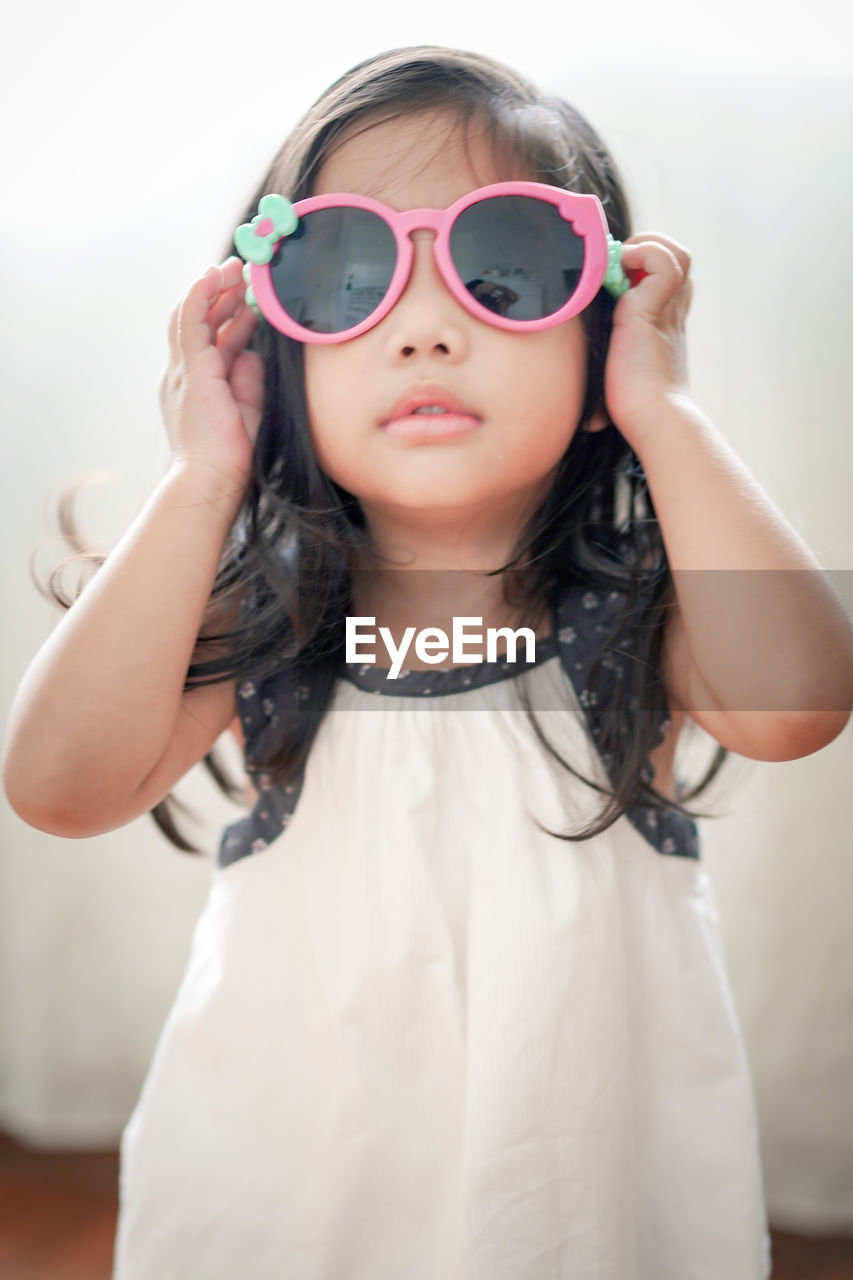 Portrait of cute girl wearing sunglasses while standing against curtain