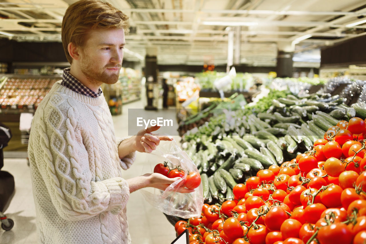 Young man buying fresh tomatoes at supermarket