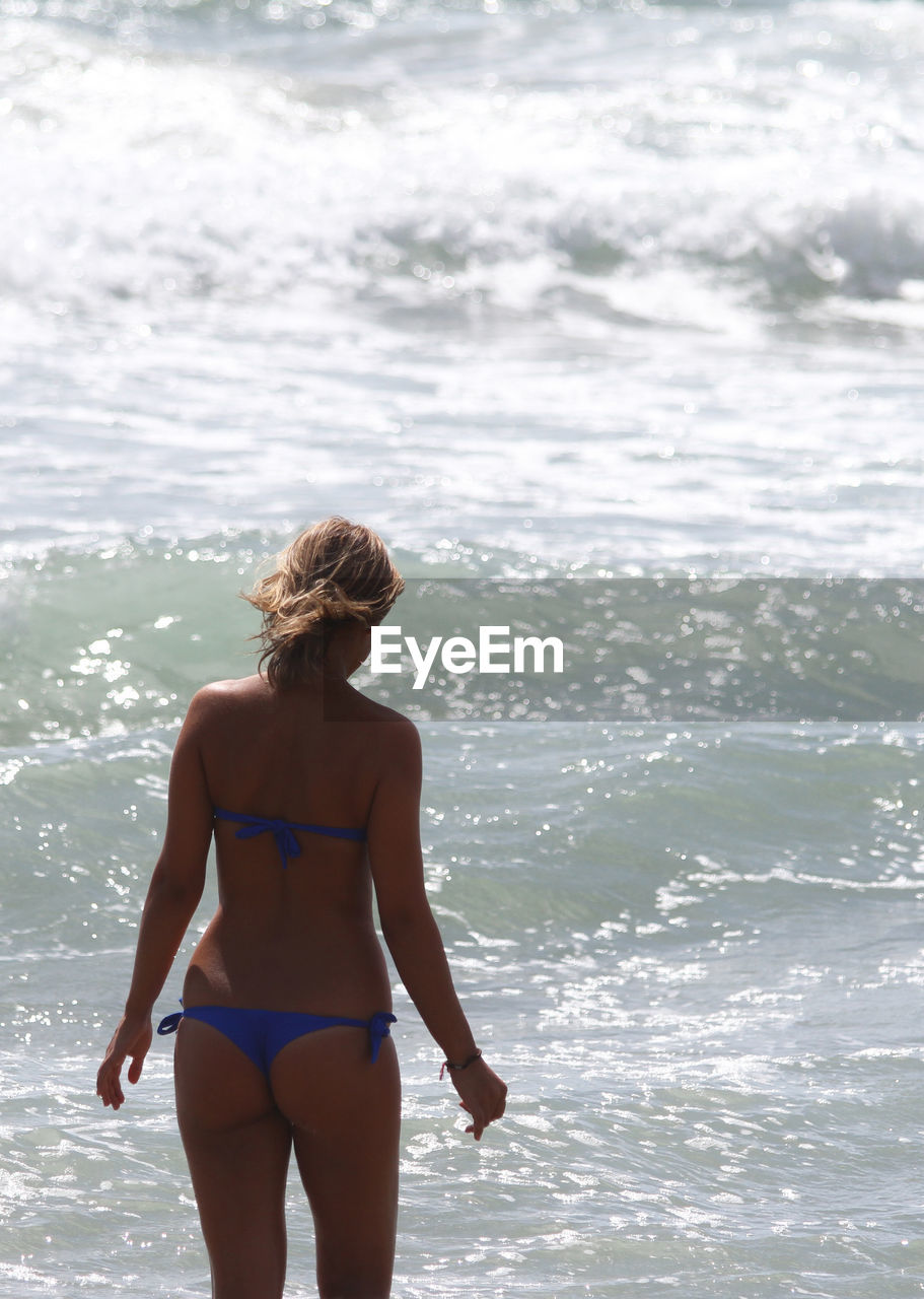 Rear view of woman wearing bikini standing in sea during sunny day