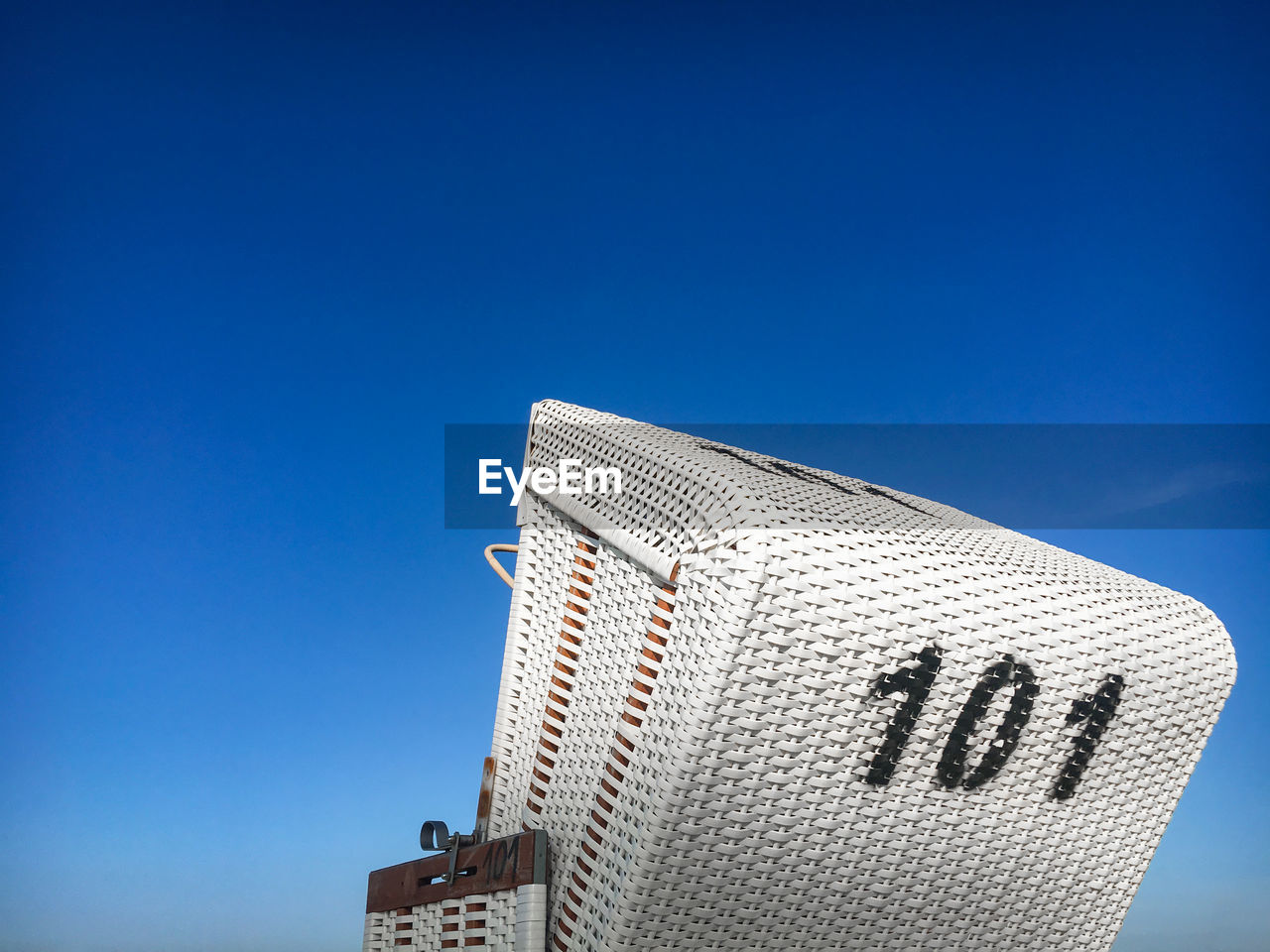 Traditional north german white beach chair with black number 101 at north sea beach against blue sky