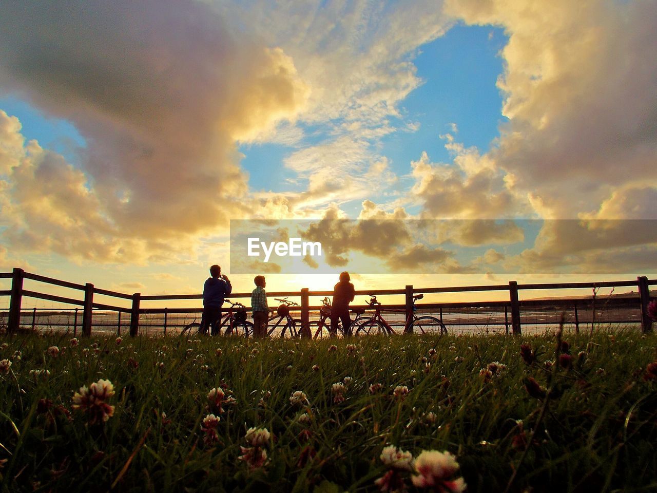 People on land against cloudy sky during sunset