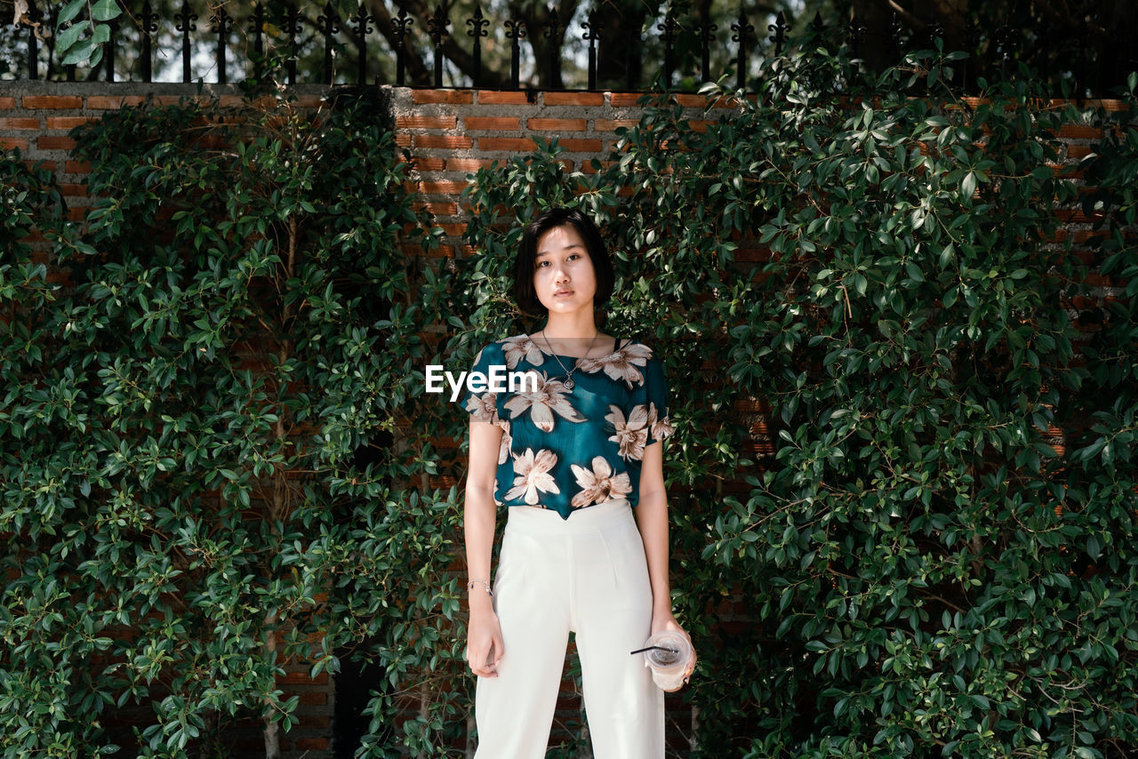 Portrait of smiling young woman standing against plants