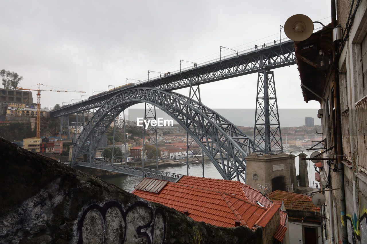 LOW ANGLE VIEW OF BRIDGE OVER RIVER IN CITY AGAINST SKY