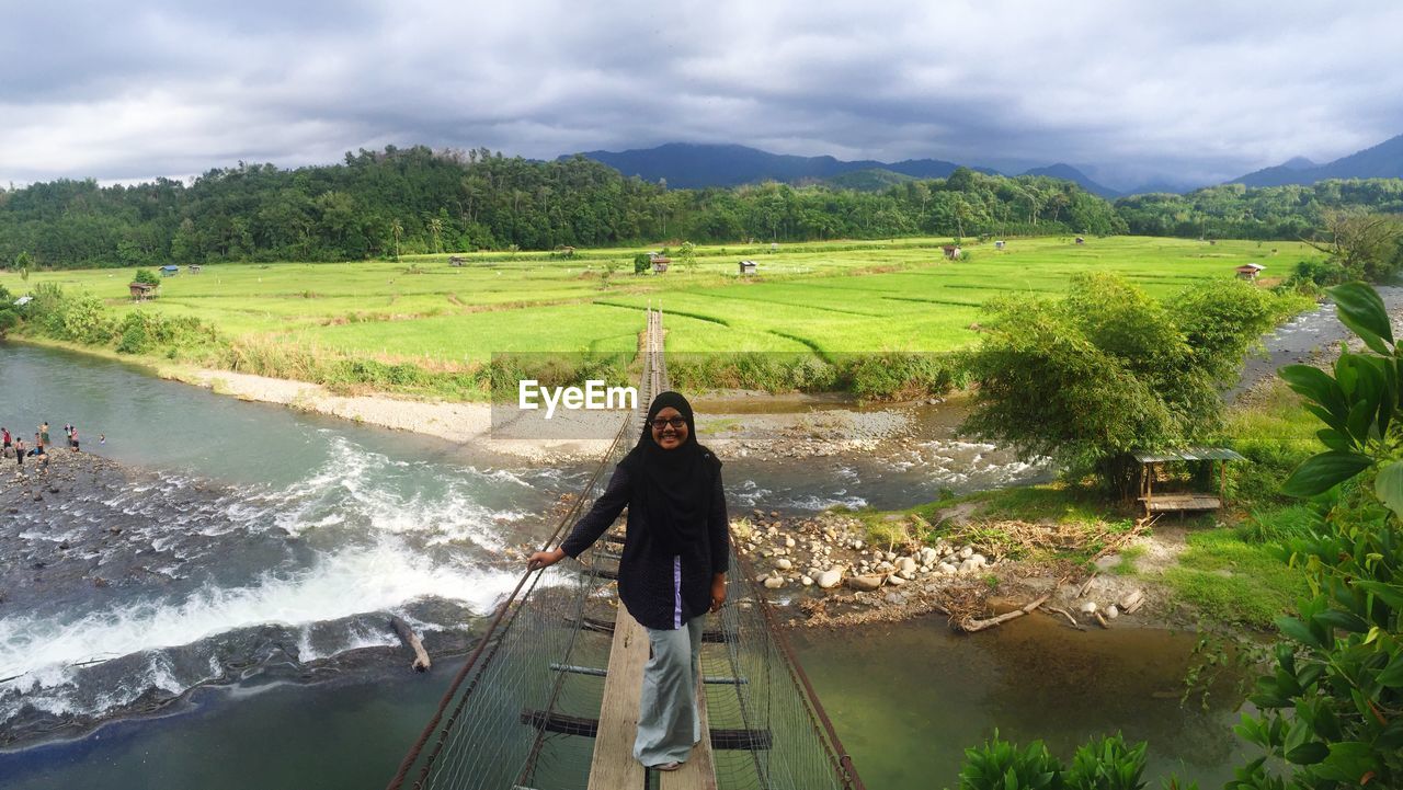 Full length portrait of smiling woman standing on over river