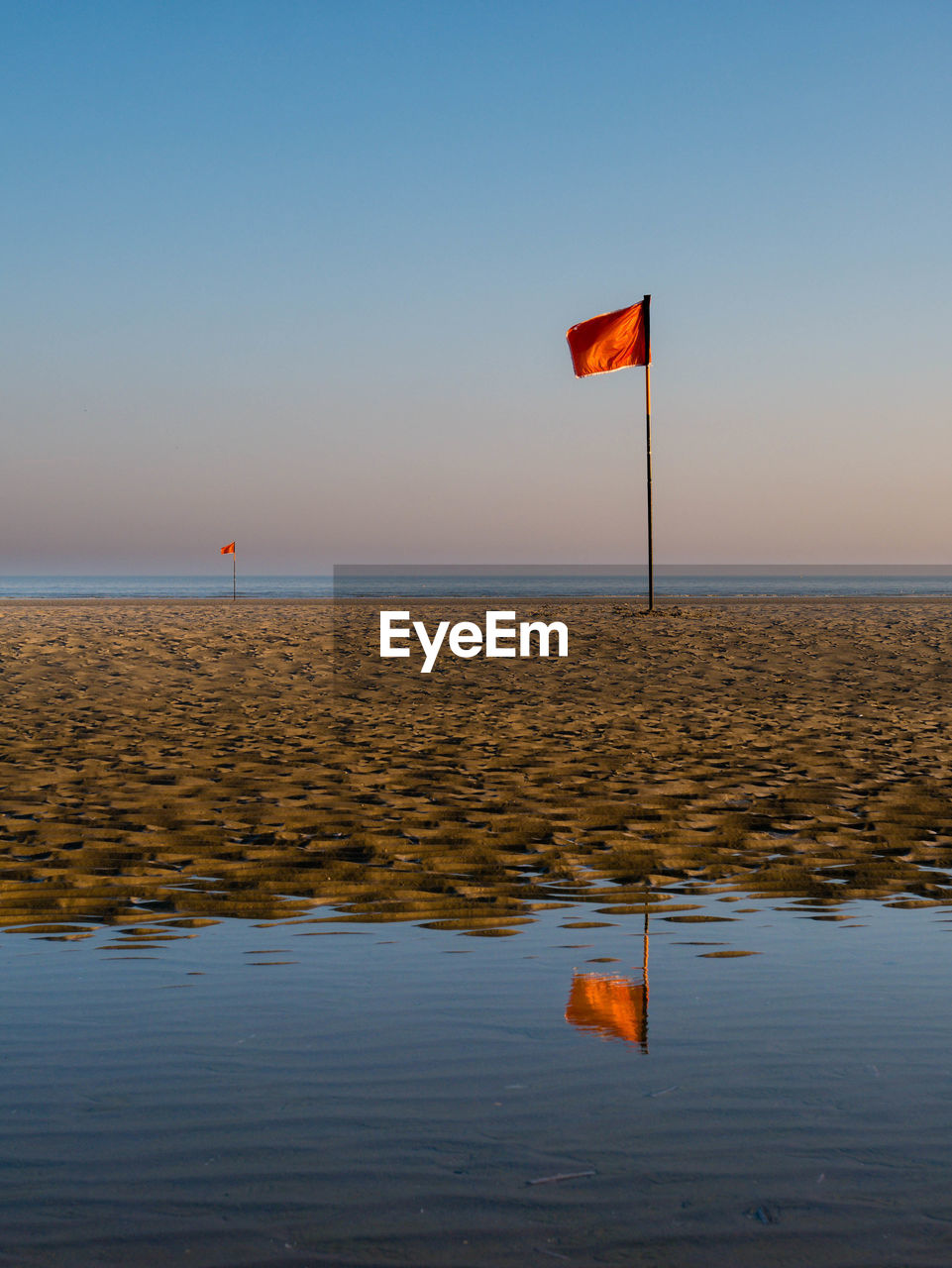 Red flag mirroring in water just after sunrise at a beach in northern france