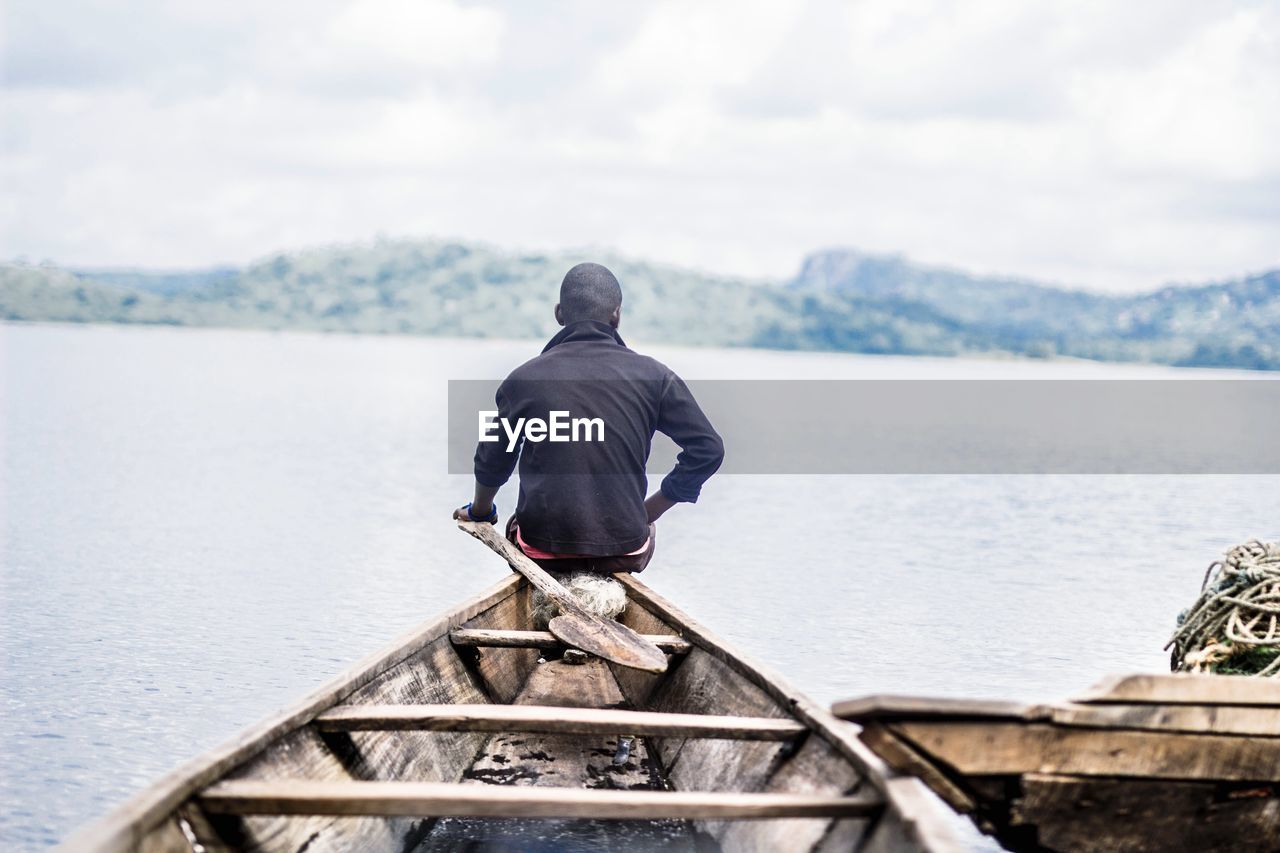 Rear view of man sitting on boat in lake against sky