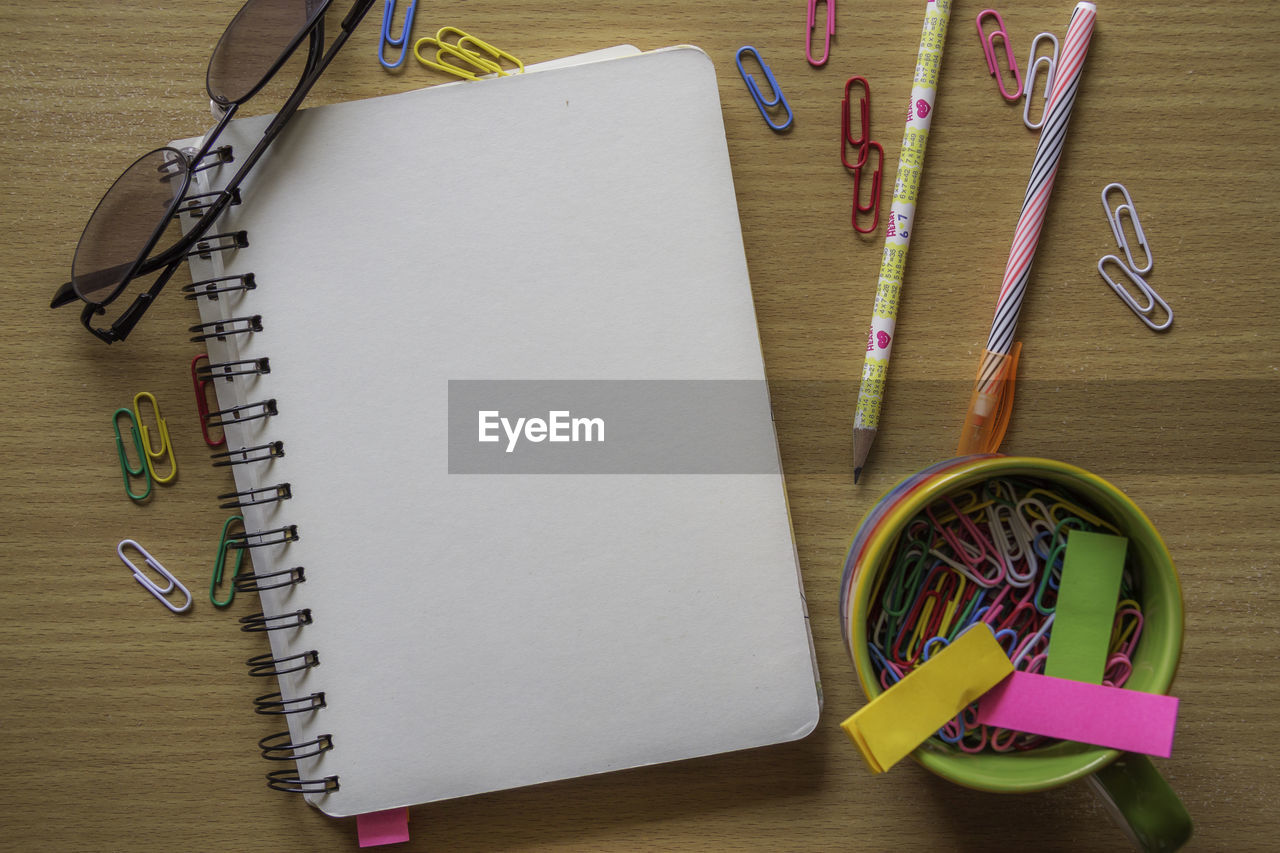 Directly above shot of blank spiral notebook and eyeglasses by school supplies on table
