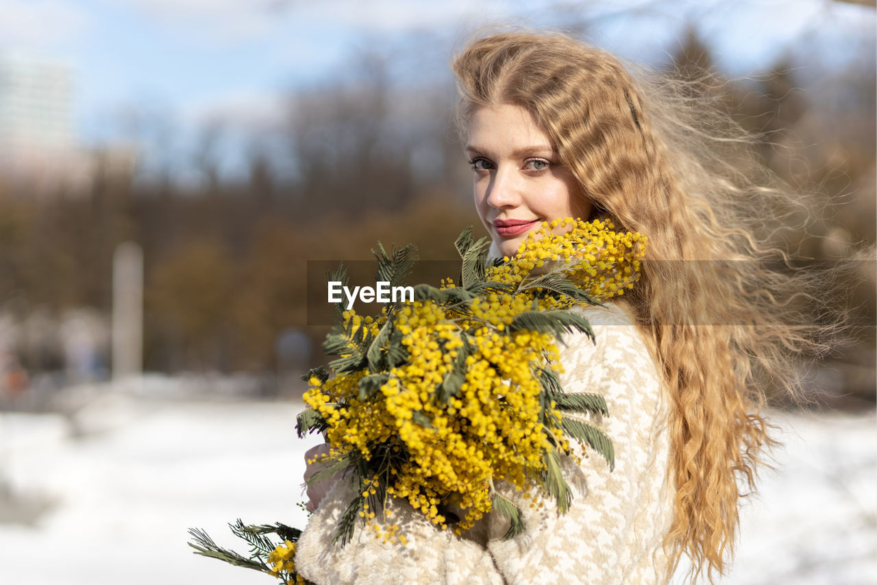 spring, winter, nature, one person, yellow, adult, women, young adult, plant, cold temperature, portrait, snow, flower, clothing, autumn, hairstyle, flowering plant, warm clothing, beauty in nature, long hair, fashion, emotion, blond hair, outdoors, smiling, tree, happiness, looking at camera, day, leisure activity, lifestyles, looking, female, focus on foreground, environment, brown hair, photo shoot, sky