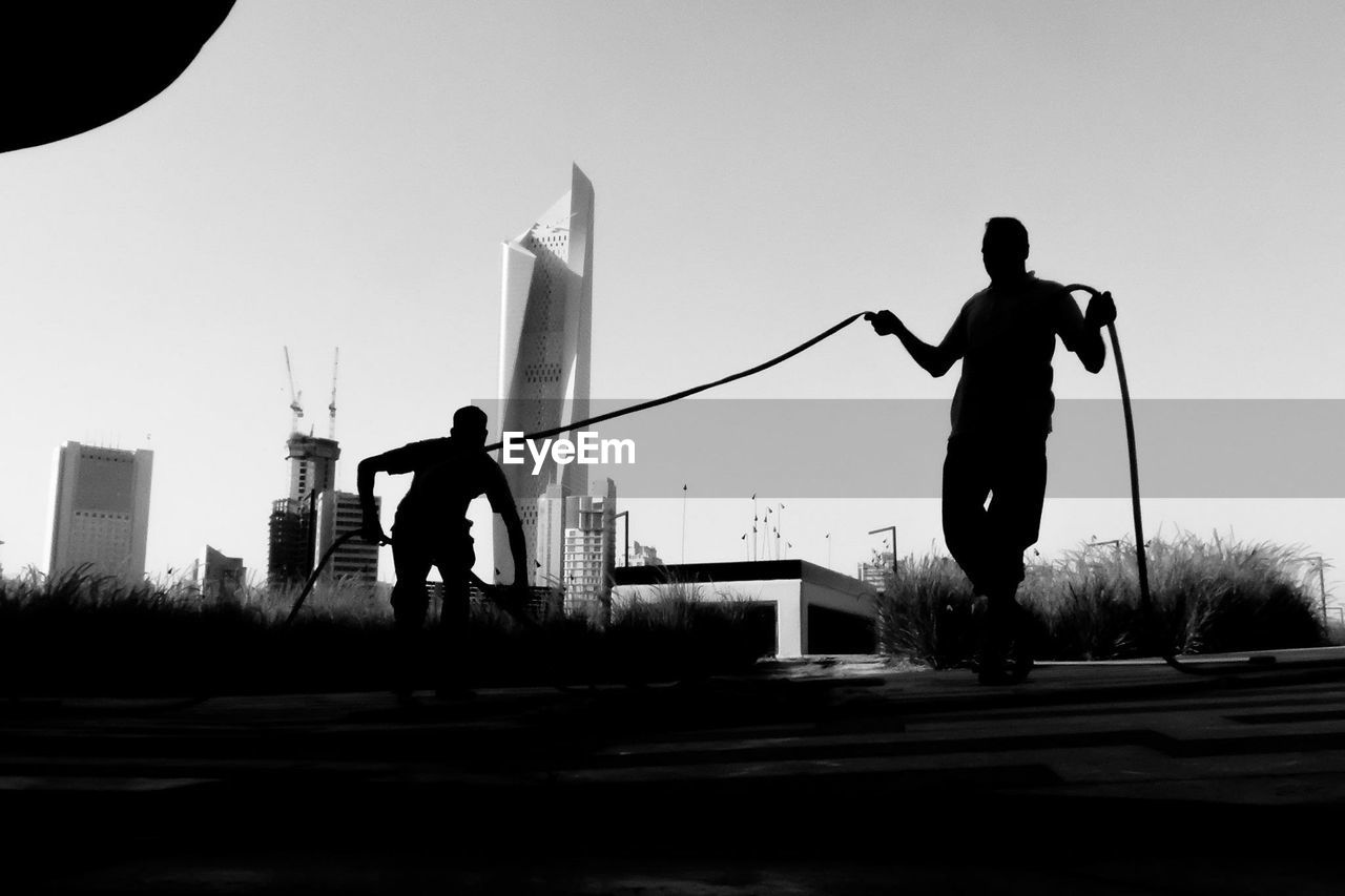 Low angle view of silhouette men with garden hose against clear sky