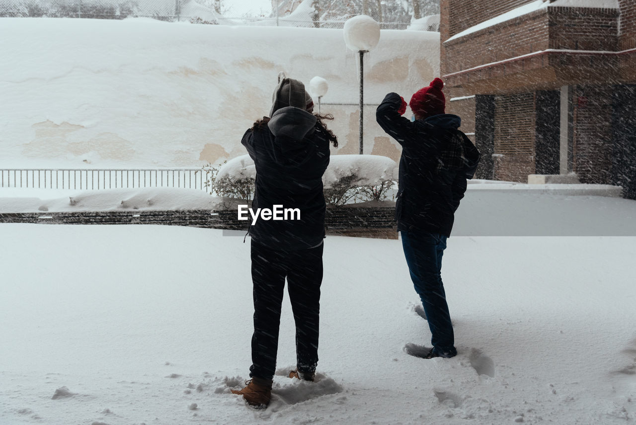 REAR VIEW OF COUPLE STANDING ON SNOW COVERED LANDSCAPE DURING WINTER