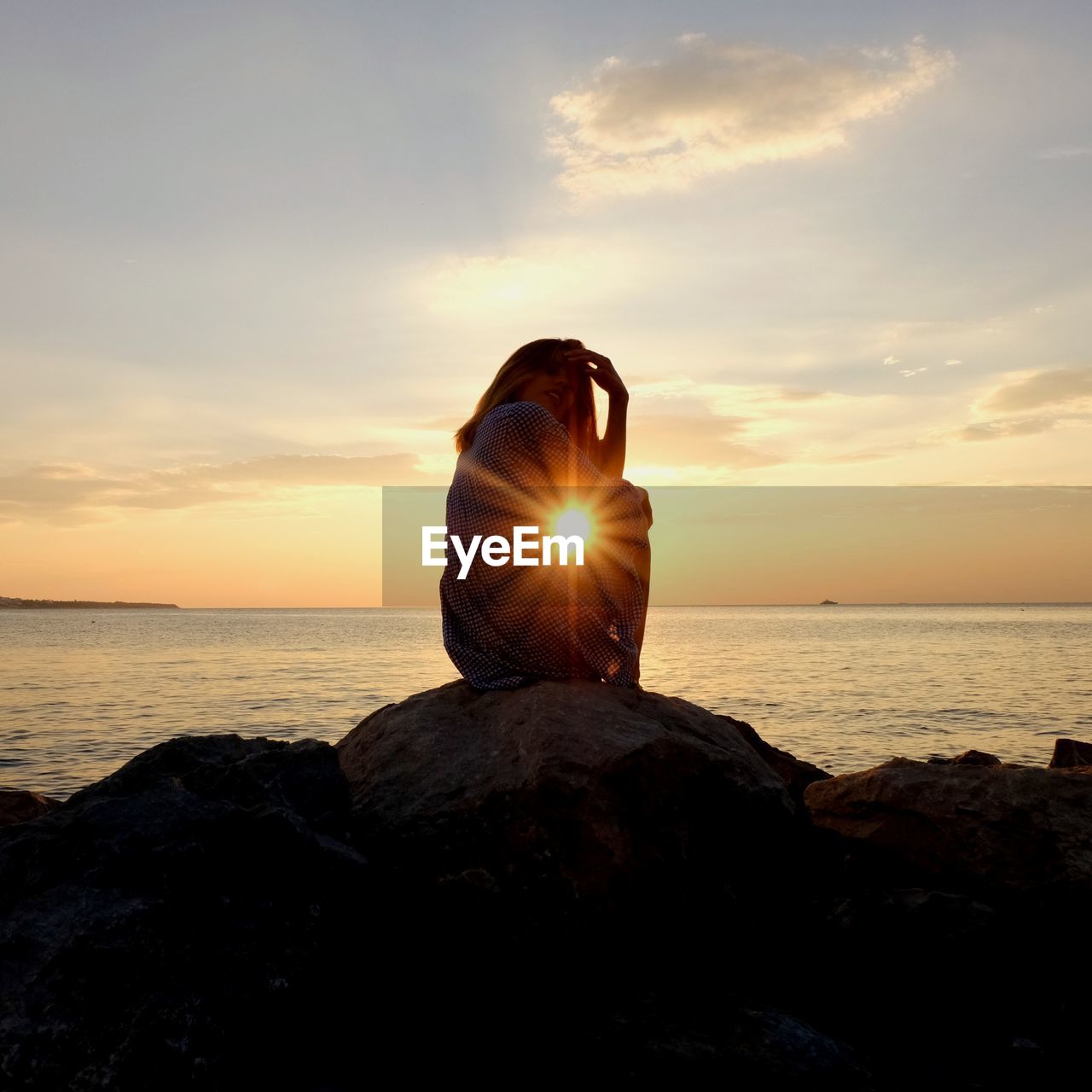 Side view of teenage girl sitting by sea against sky during sunset