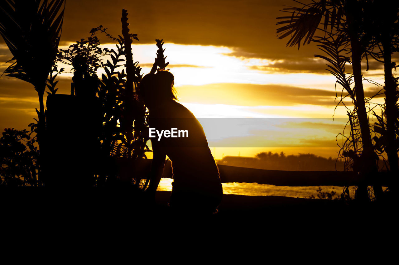 SILHOUETTE MAN STANDING BY TREES AGAINST SKY DURING SUNSET