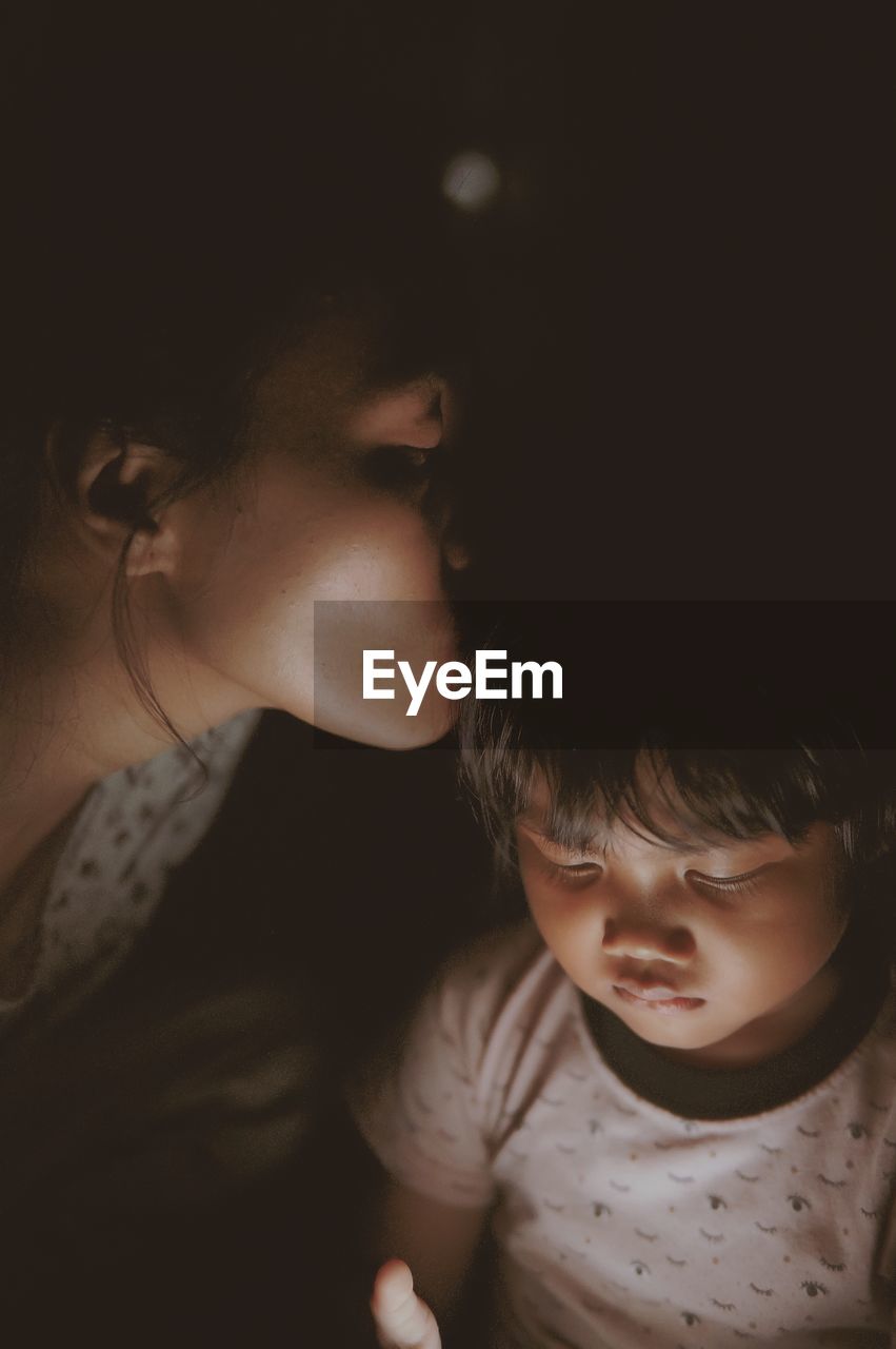 Close-up of mother kissing daughter against black background