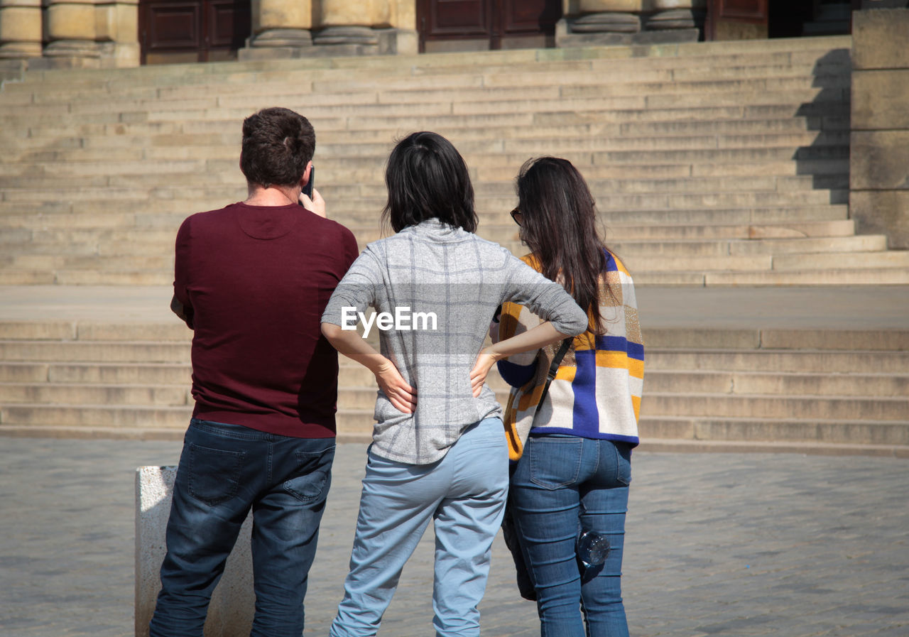 REAR VIEW OF TWO WOMEN STANDING AGAINST STAIRCASE