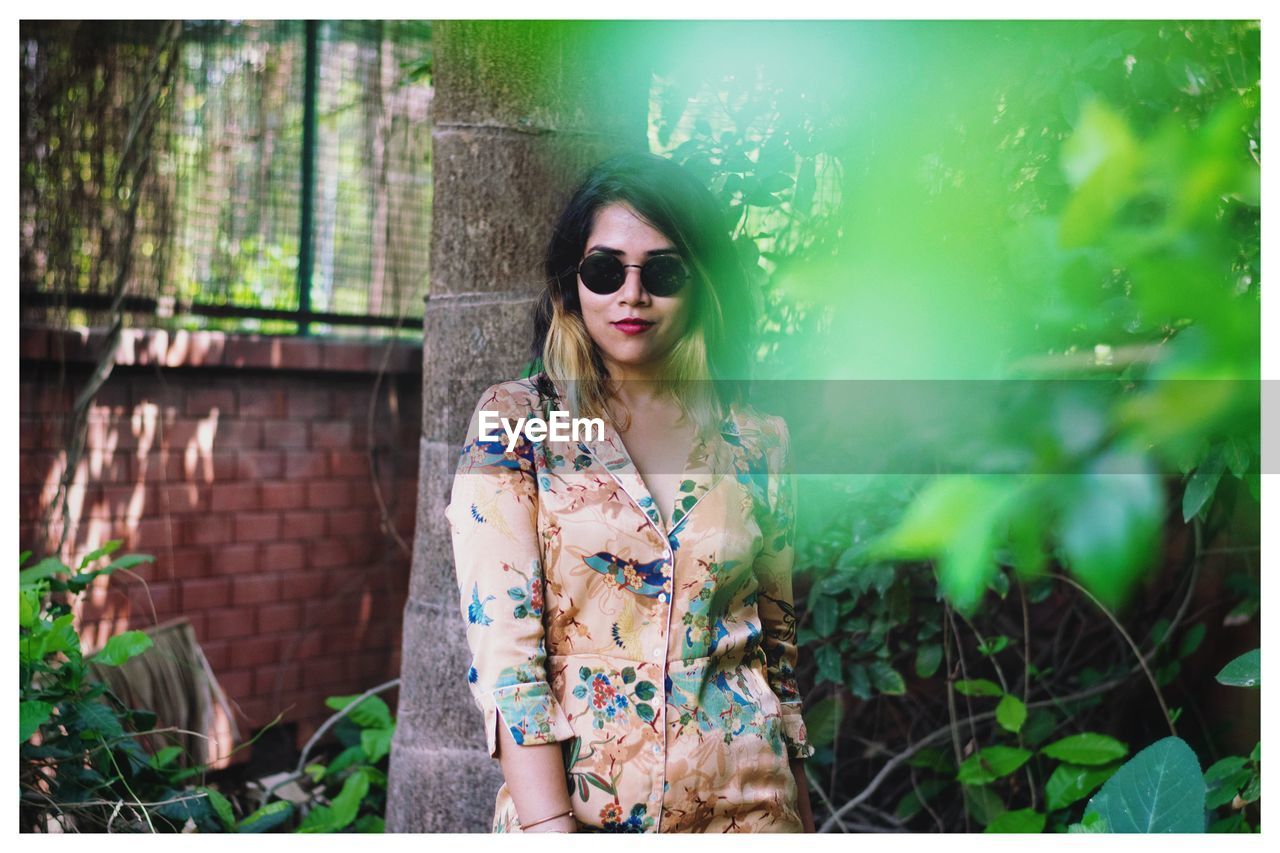 PORTRAIT OF WOMAN WEARING SUNGLASSES STANDING OUTDOORS