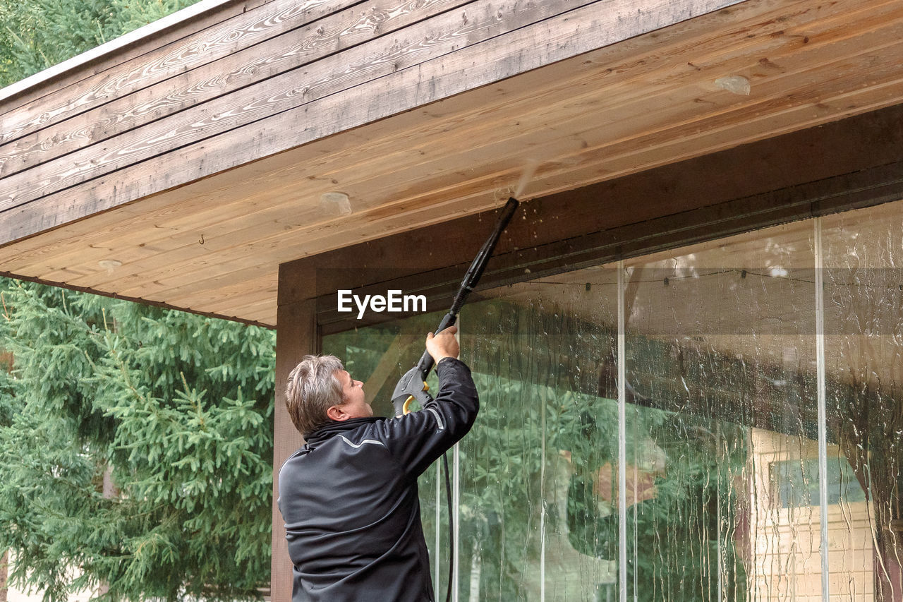 Man cleaning walls and floor with high pressure power washer. washing terrace wood planks and clad