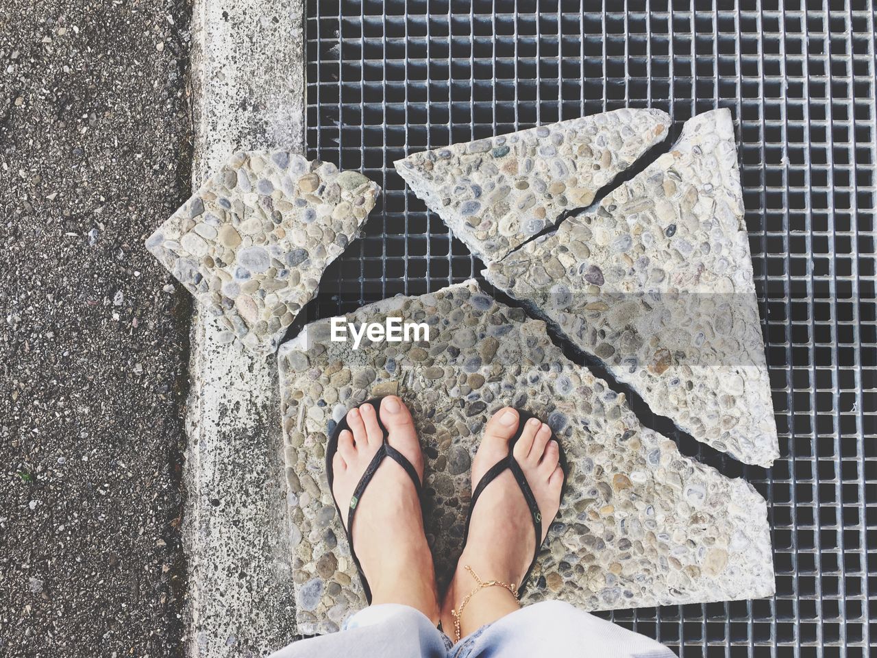 Low section of woman standing on broken stone tile over metal grate