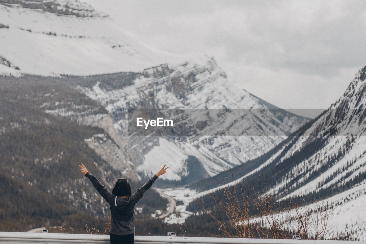 Rear view of woman with arms raised looking at snowcapped mountain