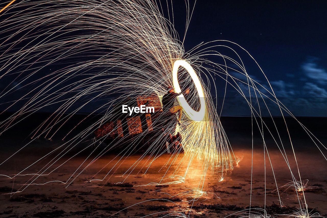 Man with wire wool at beach against sky