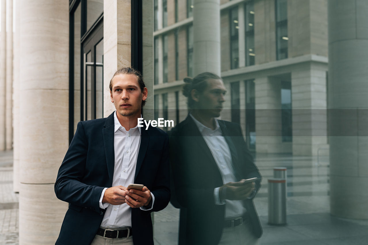 Businessman using smart phone while standing by window