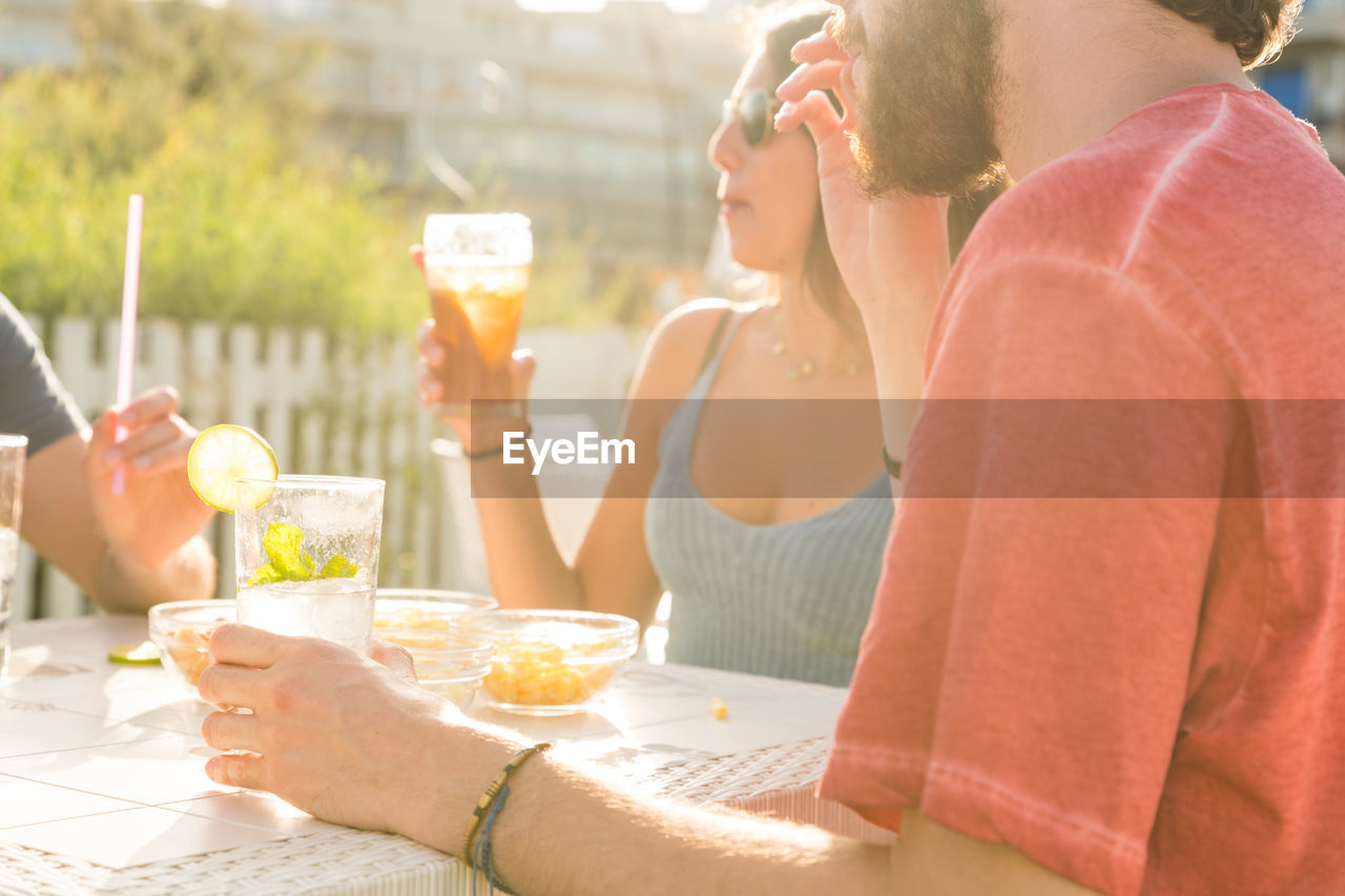 MIDSECTION OF WOMAN DRINKING GLASS ON TABLE AT CAFE