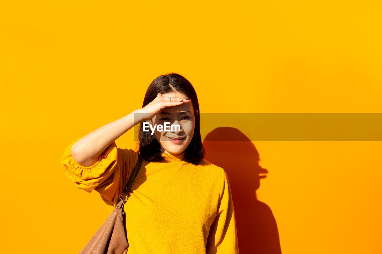 Portrait of woman shielding eyes against yellow wall