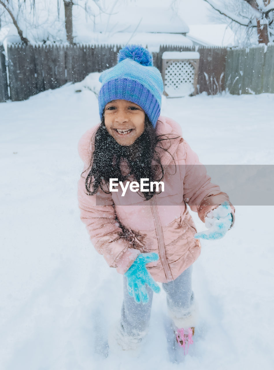 Diverse mixed race pre school toddler girl outdoors in winter playing with snow 