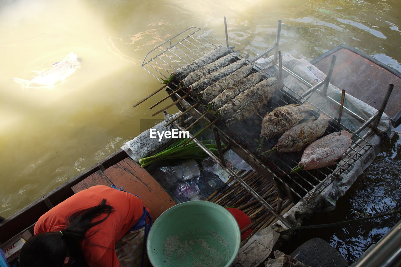 High angle view of woman by food on barbecue in boat at lake
